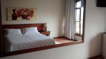 Un dormitorio con una cama, una mesita de noche, una lámpara, un cuadro y una ventana.