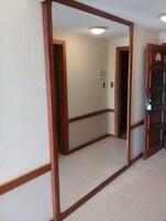 Um corredor com um espelho de madeira, soalho em azulejos e uma porta que dá para outro quarto.