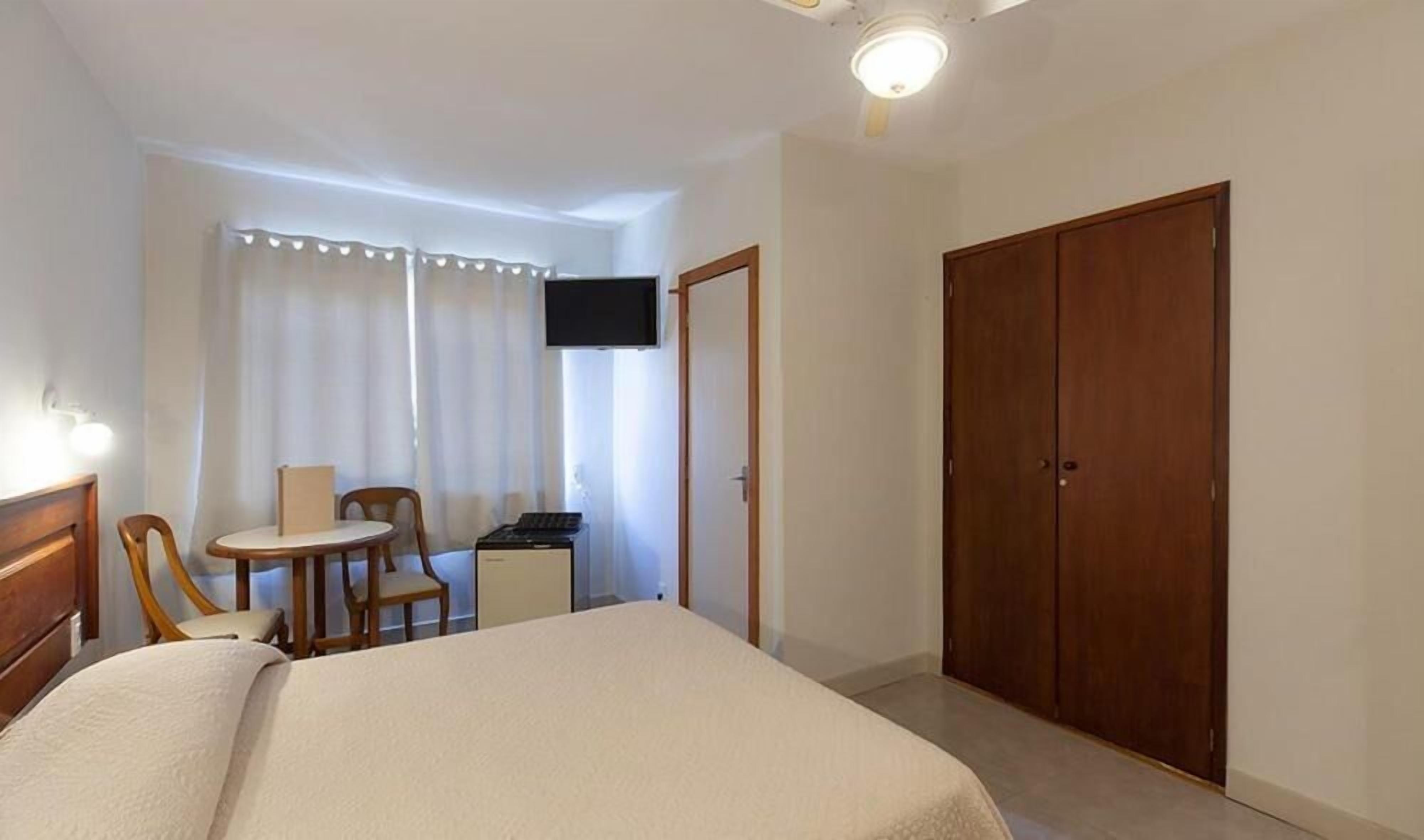 Una habitación de hotel con cama, escritorio, silla, televisor y armario.