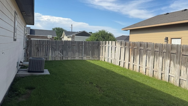 A backyard with a wooden fence, a lawn, and a building with a garage.