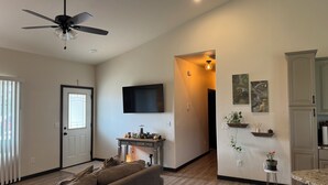 A living room with a sofa, a ceiling fan, and a TV mounted on the wall.