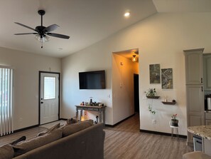 A living room with a sofa, a ceiling fan, and a TV mounted on the wall.