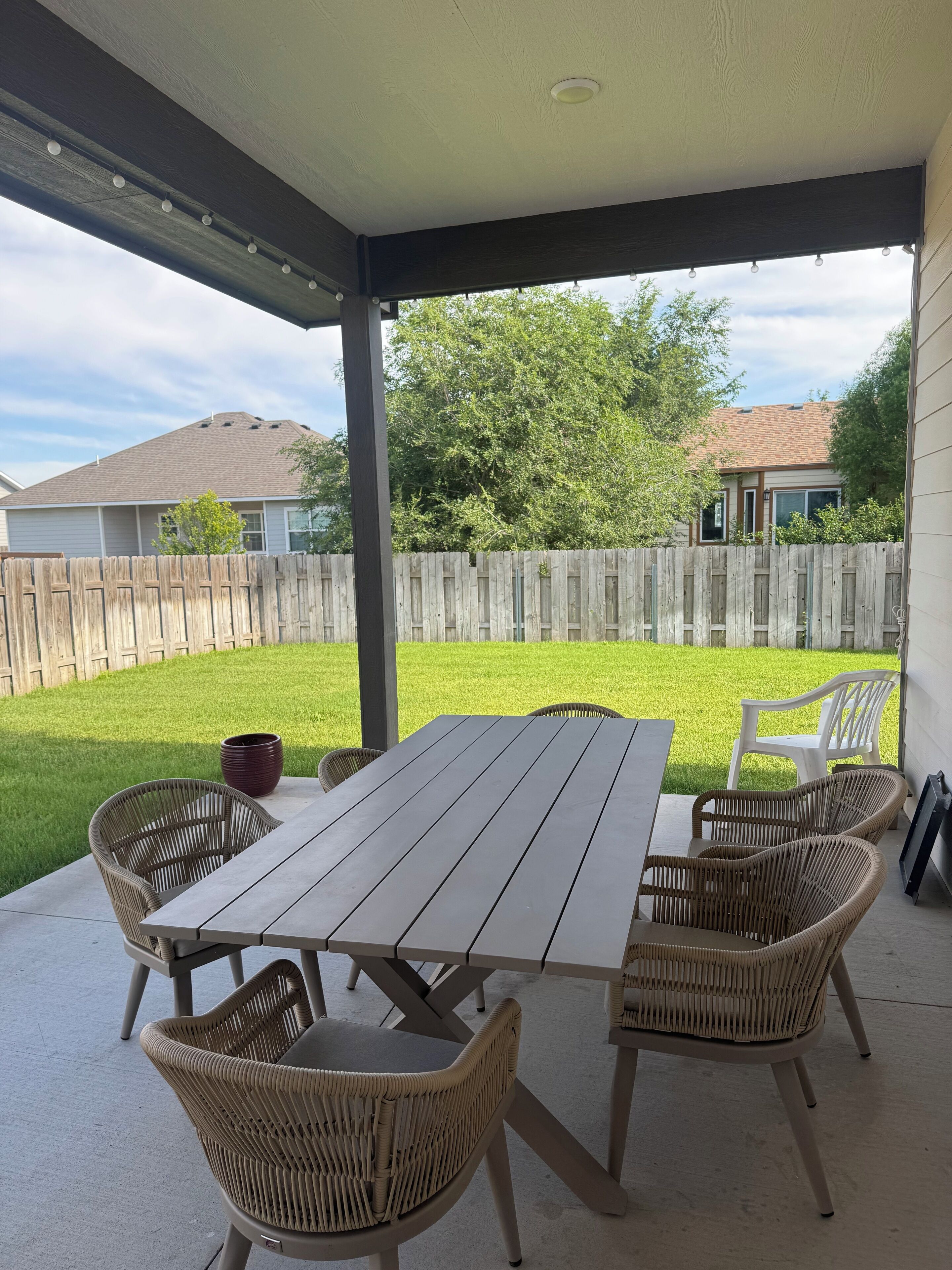 Eine überdachte Terrasse mit Tisch und Stühlen, ein Holzzaun und eine Rasenfläche.