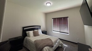A bedroom with a bed, nightstands, a window with blinds, and a ceiling light.
