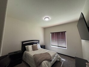 A bedroom with a bed, nightstands, a window with blinds, and a ceiling light.
