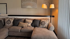 A modern living room with a sectional sofa, two wall-mounted lamps, and a large abstract painting.
