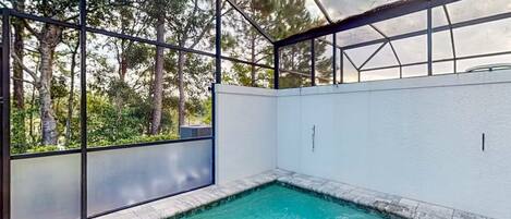 Una piscina con cerramiento de cristal, rodeada de árboles.