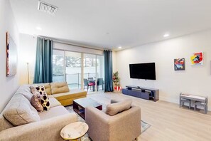 A modern living room with a sofa set, a coffee table, a flat-screen TV, and artwork on the wall. - Private Pool & Patio  3BR Family Oasis By Disney (Clermont)
