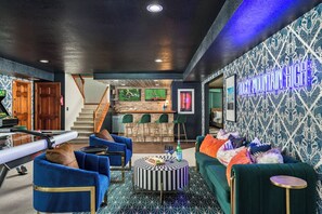 A modern living room with a bar area, a staircase, and a neon sign on the wall.