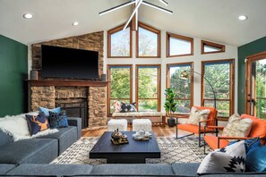 A spacious living room with a stone fireplace, large windows, and modern furniture.