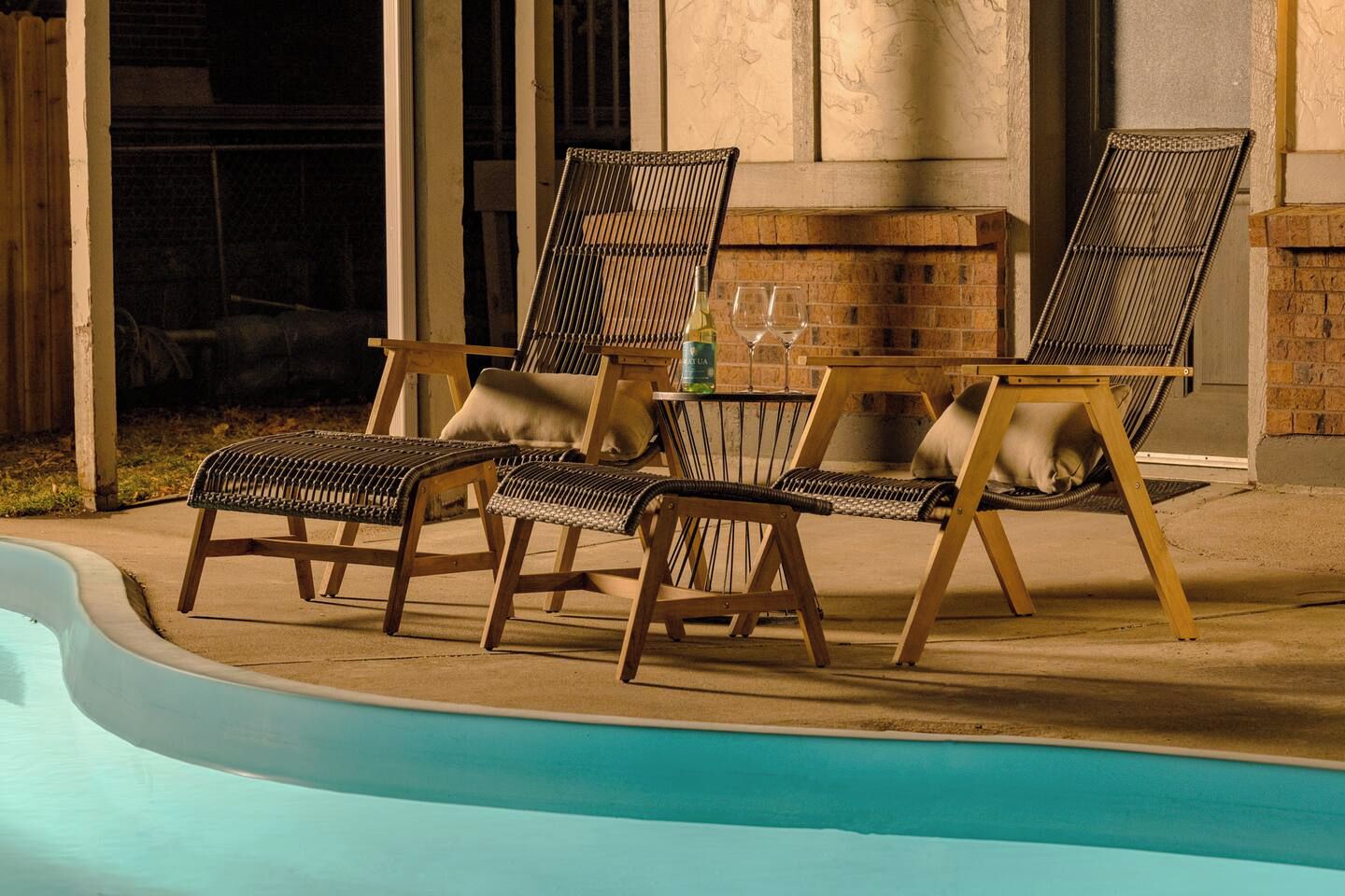 Un espace aménagé au bord de la piscine, avec des chaises longues et une table, une cheminée en briques et une vue dégagée sur la piscine.