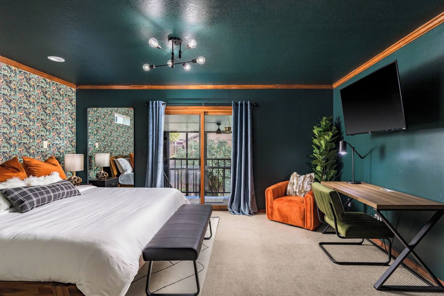Une chambre à coucher comprenant un lit, un bureau, une chaise, un téléviseur et un balcon avec des rideaux.