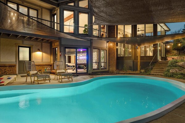 A modern house with a swimming pool, outdoor seating, and a staircase leading to the upper floor.