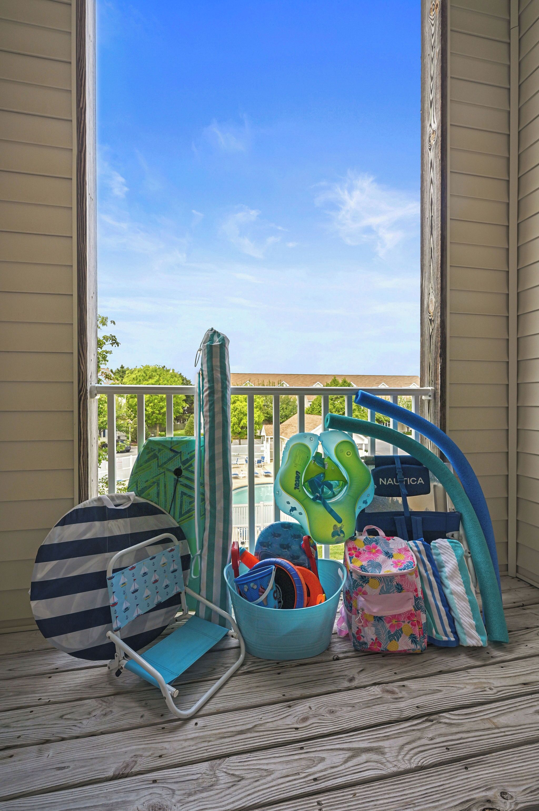 A balcony with a view of a swimming pool, a baby swing, a stroller, and a baby carrier.