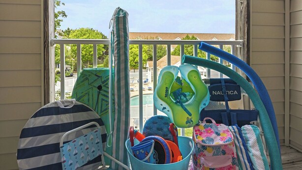 Ein Balkon mit Blick auf einen Swimmingpool, einer Babyschaukel, einem Kinderwagen und einer Babytrage.