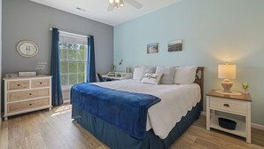Ein Schlafzimmer mit Bett, Nachttisch, Schminktisch, Deckenventilator und einem Fenster mit Vorhängen.