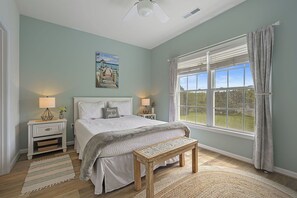 Ein Schlafzimmer mit einem Bett, zwei Nachttischen, einer Bank, einem Fenster mit Vorhängen und einem Bild an der Wand.