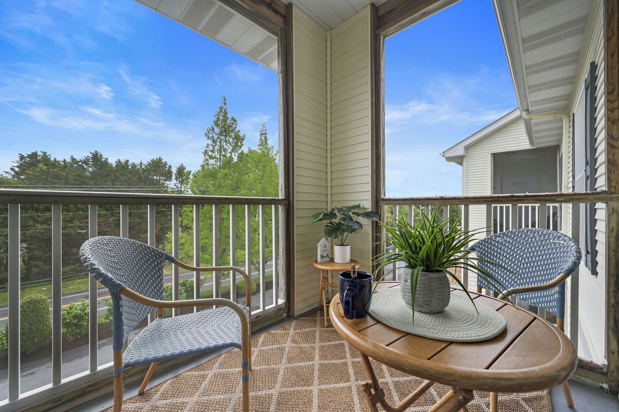 A balcony with two wicker chairs, a small table, and a potted plant.