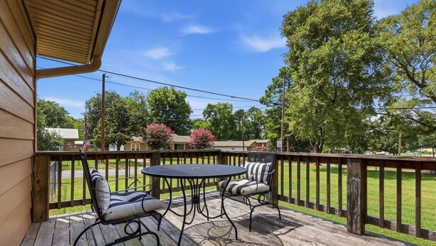 Eine Terrasse im Freien mit Tisch und zwei Stühlen, umgeben von einer Holzterrasse und einem Geländer.