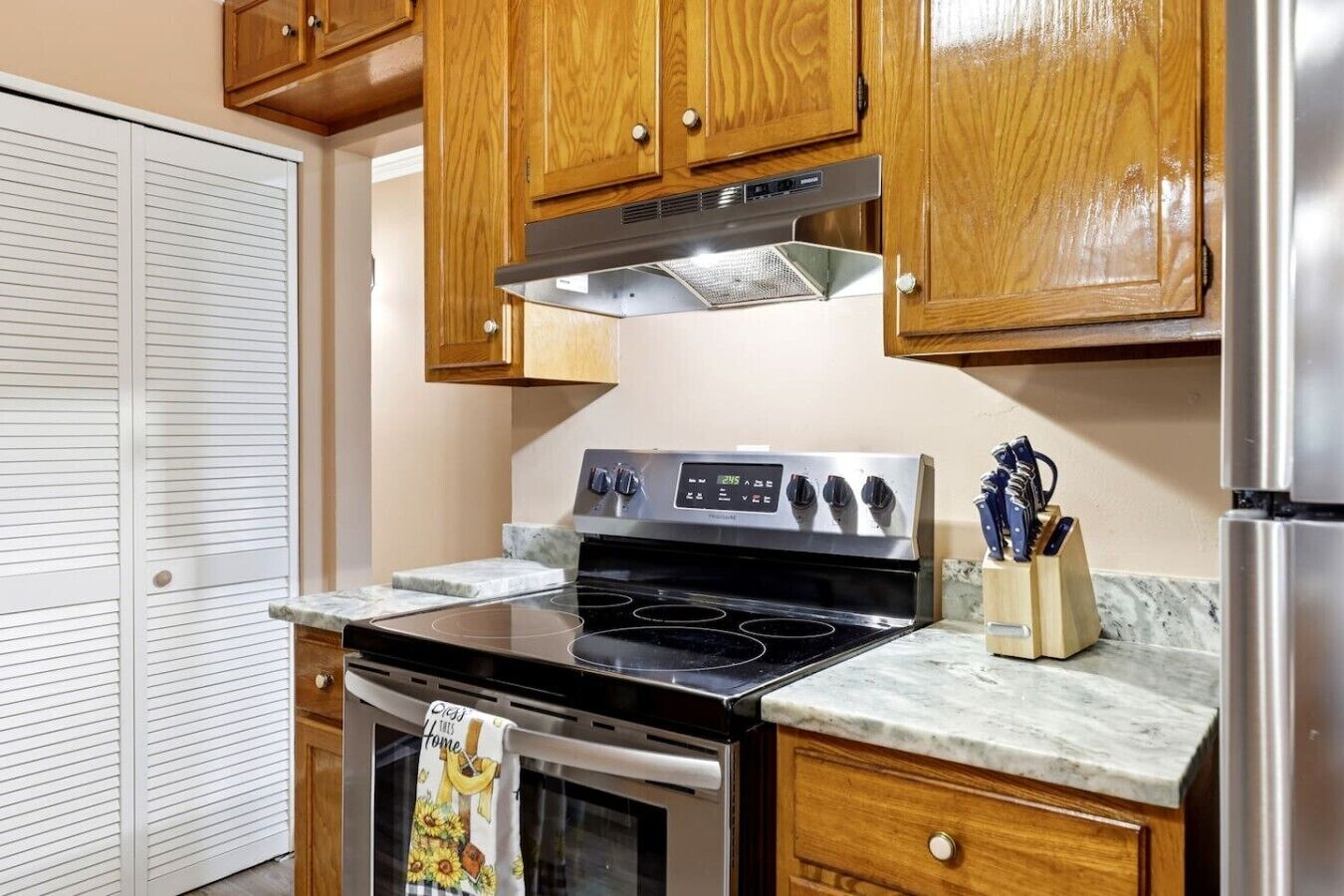 Una cocina con gabinetes de madera, estufa de acero inoxidable y encimera de mármol.
