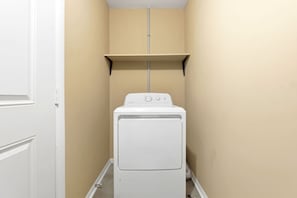 A laundry room with a front-loading washer and dryer, a beige wall, and a white door. - 6 Mi to Dtwn: Charming Home Little Rock (Little Rock)