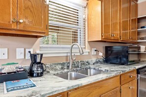 Una cocina con armarios de madera, un lavamanos de acero inoxidable, una cafetera y un microondas.