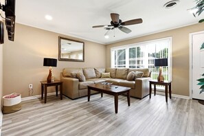 A living room with a sofa, coffee table, and two side tables, a ceiling fan, and a large window with blinds. - 6 Mi to Dtwn: Charming Home Little Rock (Little Rock)