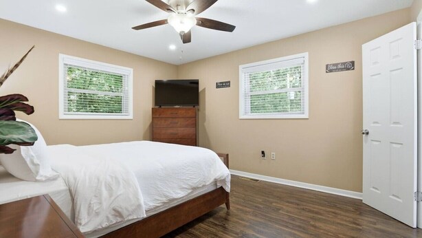 A bedroom with a bed, a ceiling fan, a dresser, a TV, and two windows with blinds. - Peaceful North Little Rock Home w Backyard! (North Little Rock)