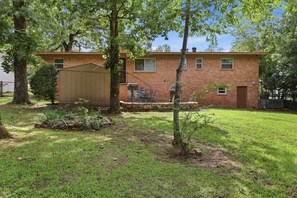A brick building with a covered patio area, surrounded by trees and grass. - Peaceful North Little Rock Home w Backyard! (North Little Rock)