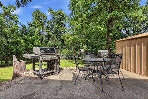 Een terras buiten, met een barbecue, een tafel en stoelen.