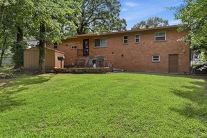 A brick house with a well-maintained lawn and a barbecue grill in the backyard.