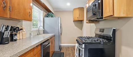 A compact kitchen with wooden cabinets, a stainless steel refrigerator, a microwave, a stove, and a dishwasher.