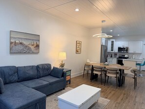 A modern living room with a gray sofa, a white coffee table, and a dining area with a wooden table and chairs. - Happy Zen Retreat - Family's Perfect Beach Retreat (Panama City Beach)