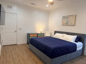 A bedroom with a bed, a nightstand, a chair, a door, and a ceiling light. - Happy Zen Retreat - Family's Perfect Beach Retreat (Panama City Beach)