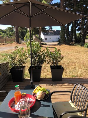 An outdoor patio with a table set for a meal, including fruits, a bottle of juice, and condiments. - Rosel Apartment, 300 meters from Kersidan Beach (Trégunc)