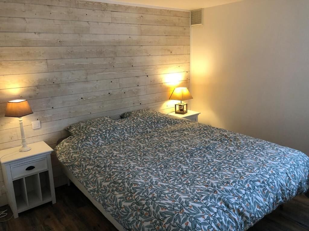 Un dormitorio con cabecera de madera, cama con colcha estampada, dos lámparas de noche y una mesita de noche con cajón.