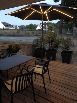 An outdoor patio with a table and chairs, a large umbrella, and potted plants. - Rosel Apartment, 300 meters from Kersidan Beach (Trégunc)