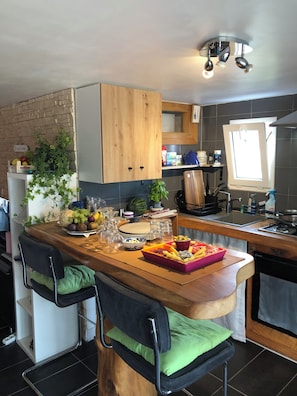A kitchen with wooden cabinets, a built-in island with seating, a window, and various kitchen appliances. - Rosel Apartment, 300 meters from Kersidan Beach (Trégunc)
