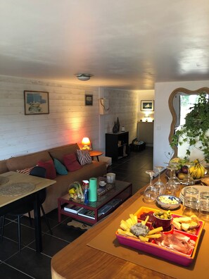 A cozy living room with a sofa, a coffee table, and a dining area with a tray of snacks and drinks. - Rosel Apartment, 300 meters from Kersidan Beach (Trégunc)