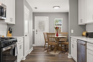 A kitchen with white cabinets, a stove, and a dining area with a table and chairs. - Charming Bungalow - Walk to Georgetown Square (Georgetown)