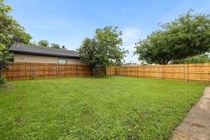 A backyard with a wooden fence, a house, and a tree. - Charming Bungalow - Walk to Georgetown Square (Georgetown)