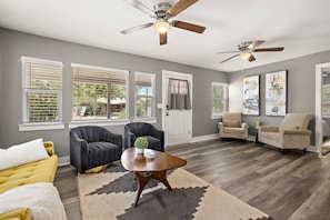 A spacious living room with a yellow sofa, two armchairs, a coffee table, and a ceiling fan. - Charming Bungalow - Walk to Georgetown Square (Georgetown)