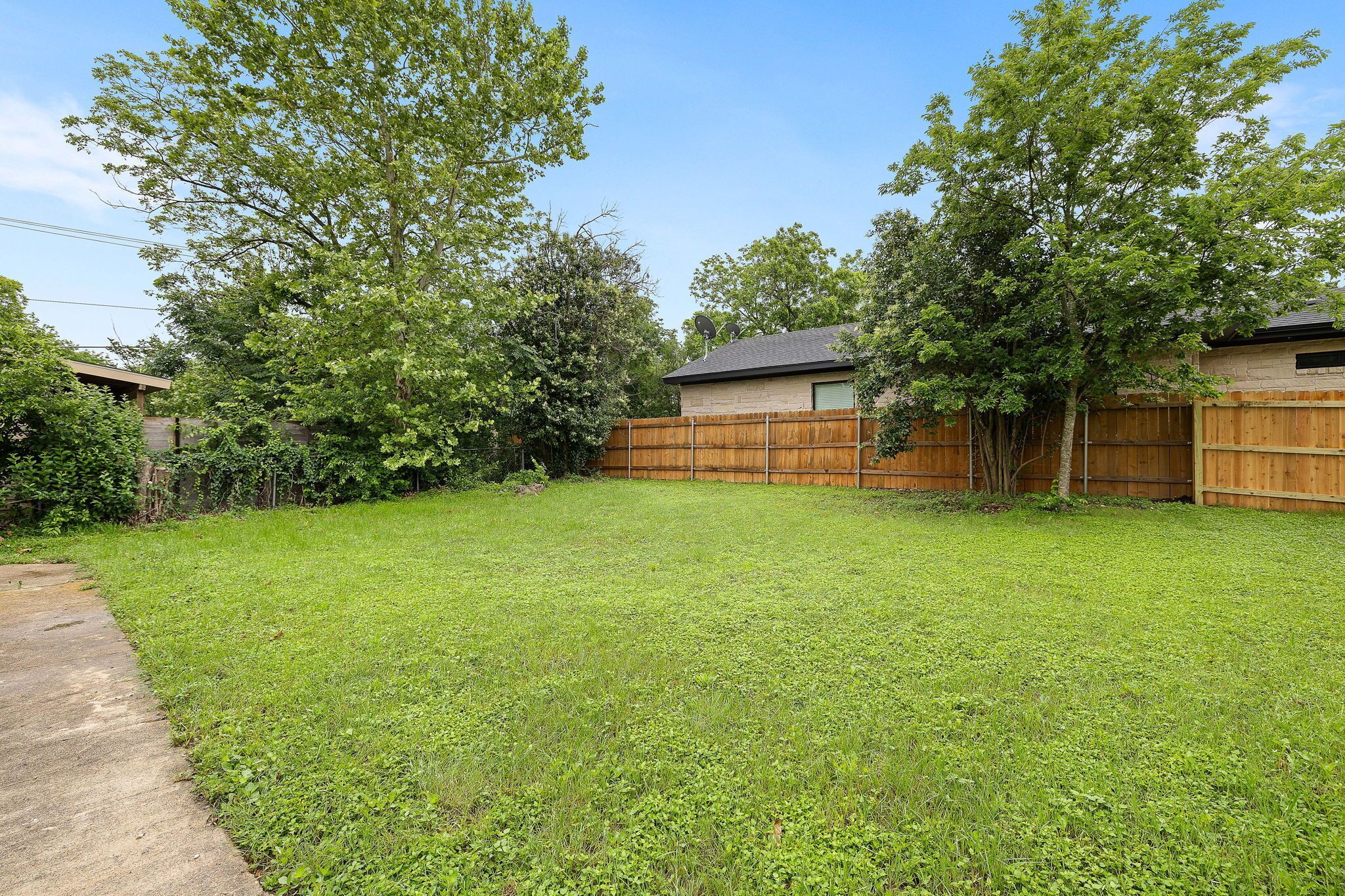A backyard with a wooden fence, a grassy lawn, and trees.