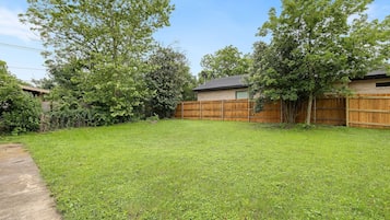 A backyard with a wooden fence, a grassy lawn, and trees.