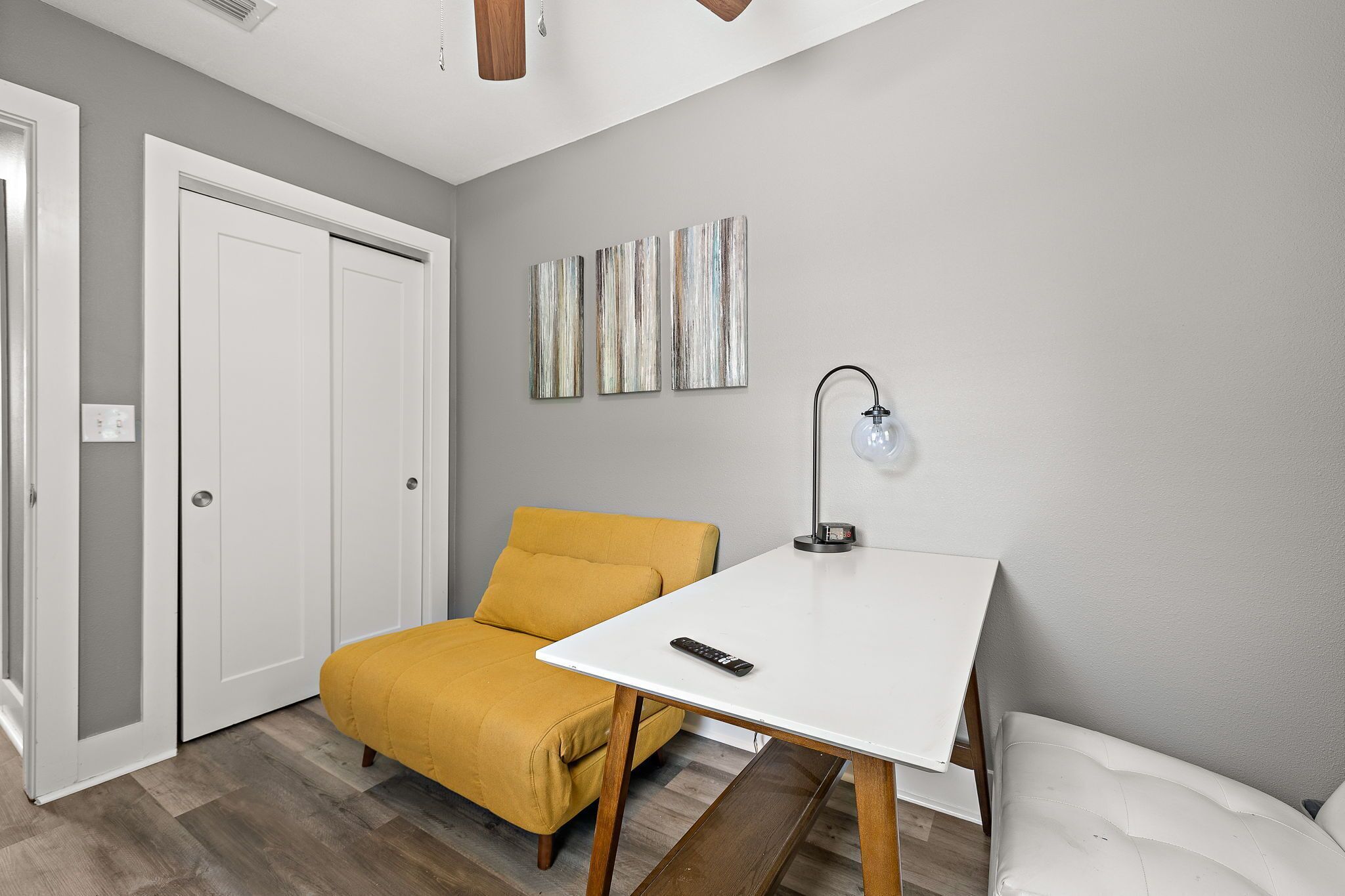 A room with a bed, a yellow sofa, a white table, and a wall-mounted lamp.