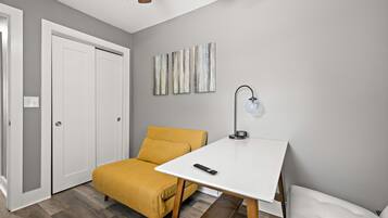 A room with a bed, a yellow sofa, a white table, and a wall-mounted lamp.