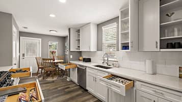 A modern kitchen with white cabinetry, a built-in dishwasher, and a dining area with a wooden table and chairs.