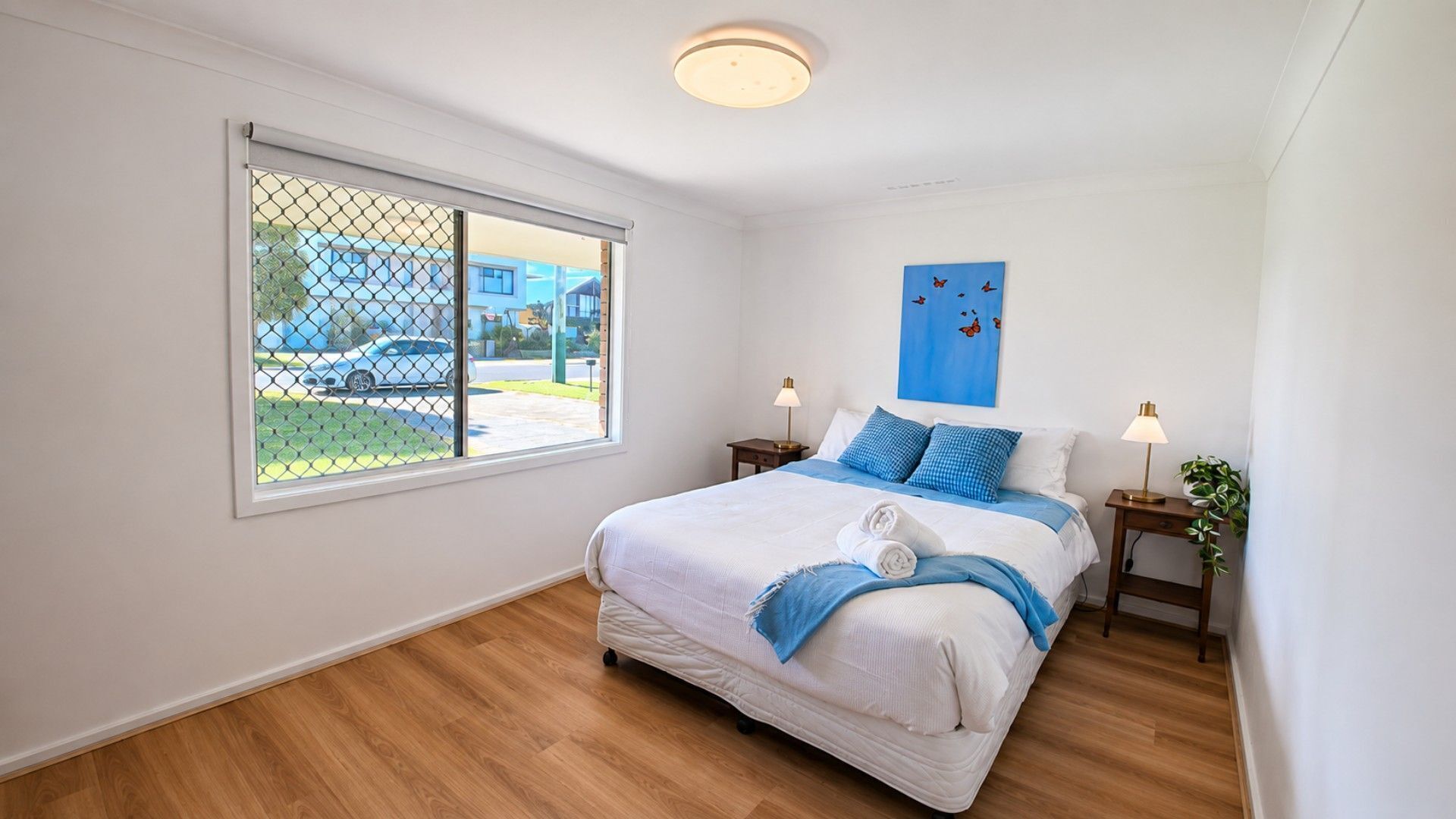 Une chambre à coucher avec un lit, deux tables de chevet, une fenêtre donnant sur un paysage agréable et un luminaire au plafond.
