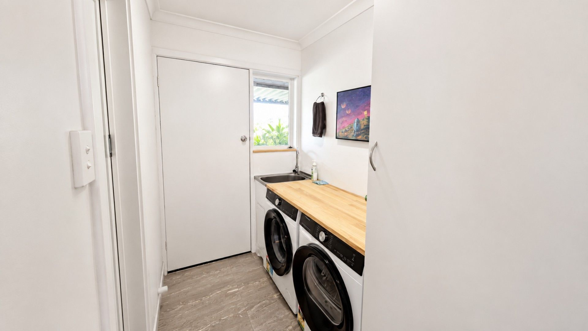 A compact laundry room with a washing machine, a dryer, a sink, and a window.