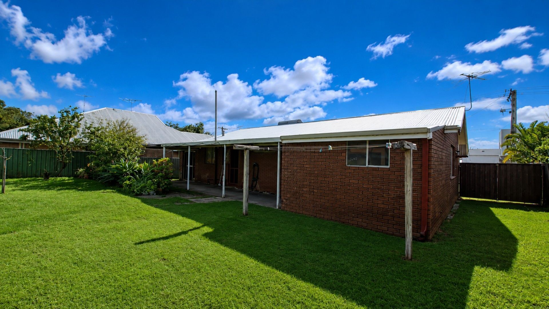A single-story brick house with a covered patio area, a fenced yard, and a clear blue sky.